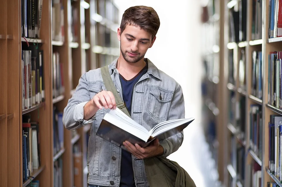 Student in Bibliothek zwischen Bücherregalen mit Buch in der Hand