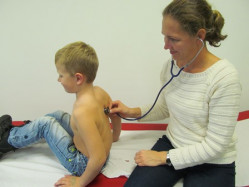 Schulärztliche Untersuchung Ärztin hört Jungen bei schulärztlicher Untersuchung mit Stethoskop ab