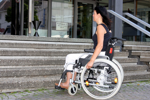 Junge Frau mit Rollstuhl vor einer Treppe