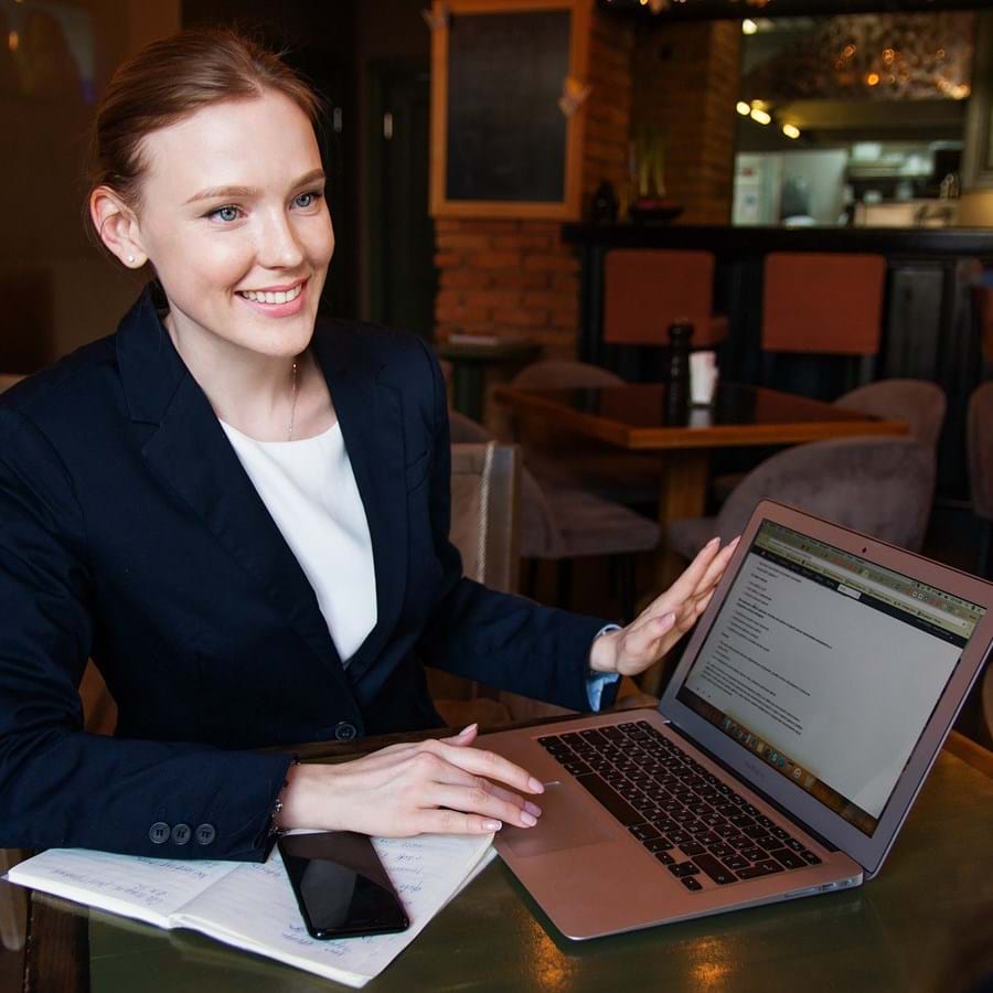 Junge Frau im Restaurant mit Laptop und Arbeitsmaterial auf dem Tisch