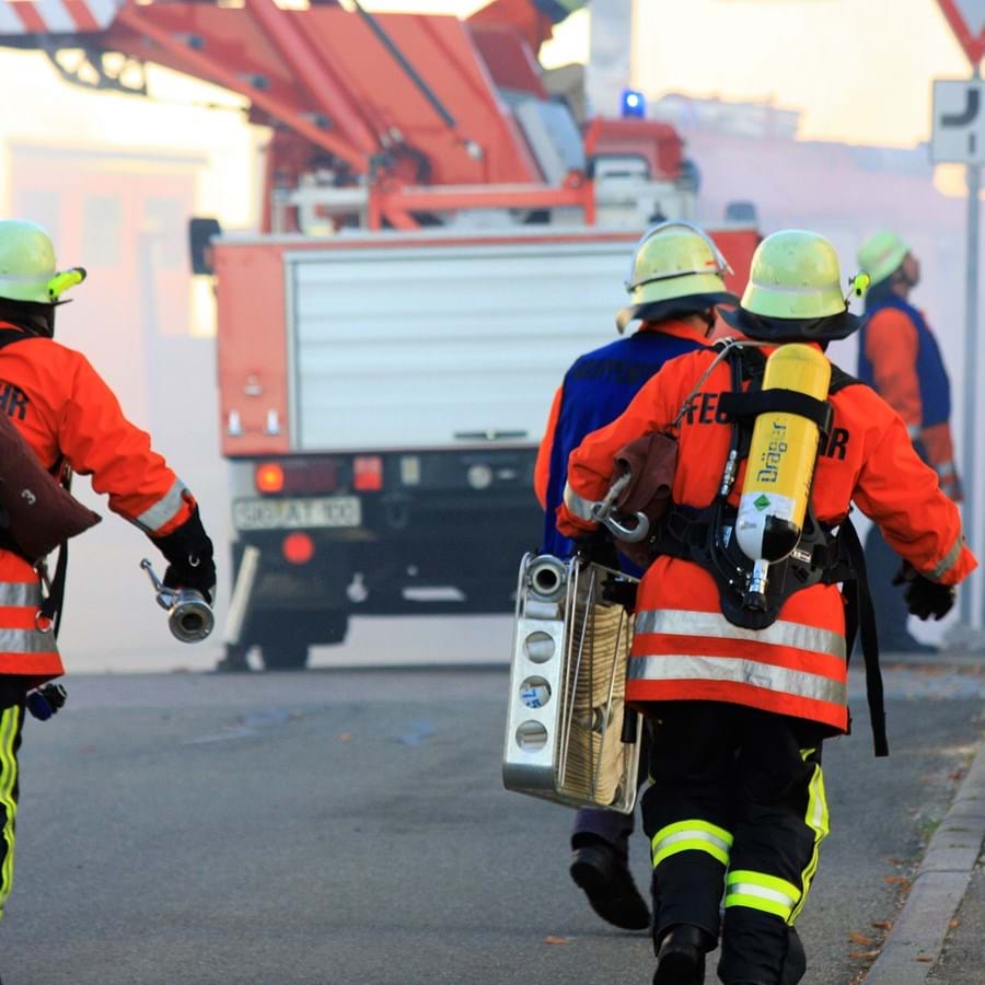 Feuerwehrleute laufen in Vollmontur und mit Ausrüstung zum Einsatzort