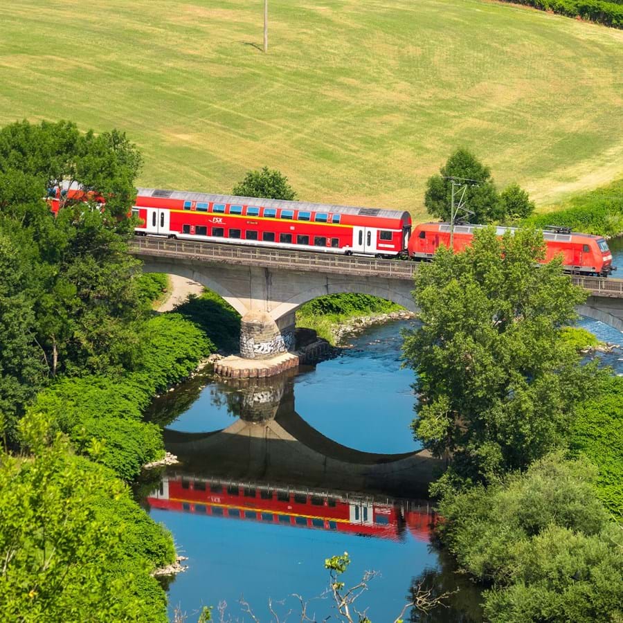 Zug fährt in idyllischer Gegend auf Bahnbrücke über einen Fluss