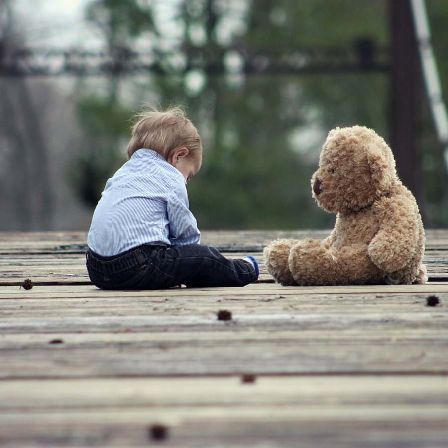 ein Kleinkind sitzt neben einem Teddybär auf einem Steg